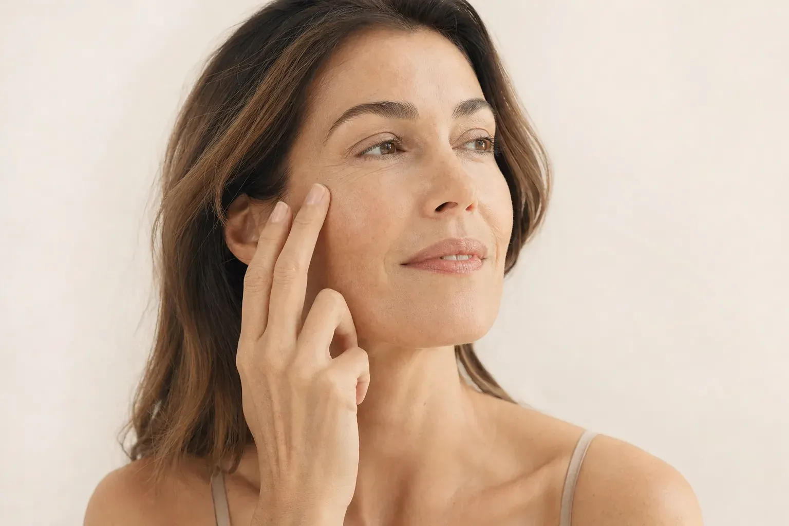 Three-quarter portrait of a woman in her forties touching her cheekbone lightly with two fingertips